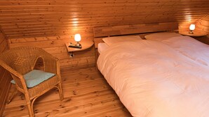 A wooden cabin room with a bed, a chair with a cushion, and two bedside lamps. - Come to This House to Stay for Holidays (Oberharz am Brocken)