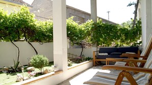 A patio with wooden chairs, a small garden with rocks and plants, and a white wall in the background. - Step Away From The Beach 1-bedroom Apartment Lolov (Preko)