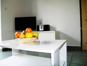 Uma mesa branca com uma tigela de frutas e um rádio.