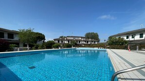 A clear swimming pool with a tiled deck, surrounded by buildings with a traditional architectural style.
