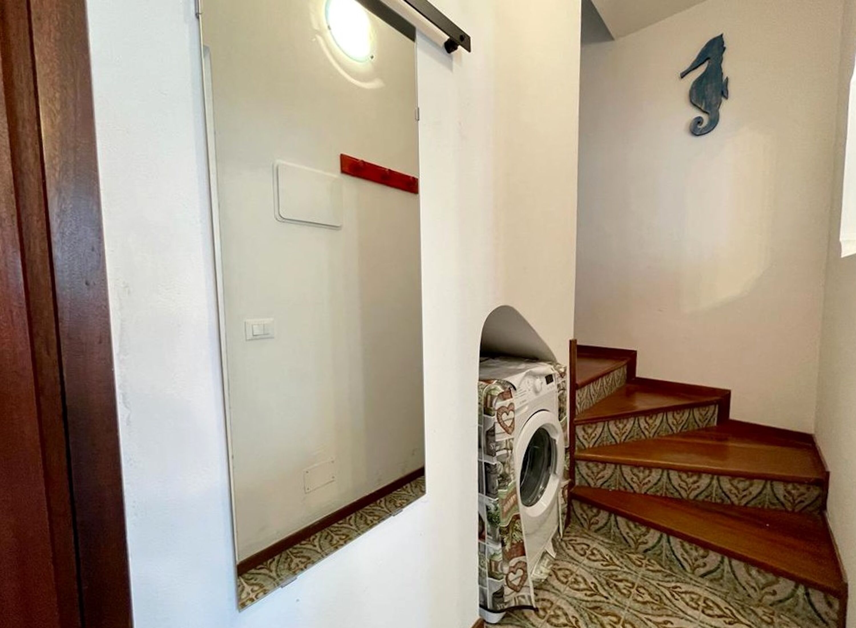A staircase with a washing machine built into the wall, a red light switch, and a seahorse decoration on the wall.