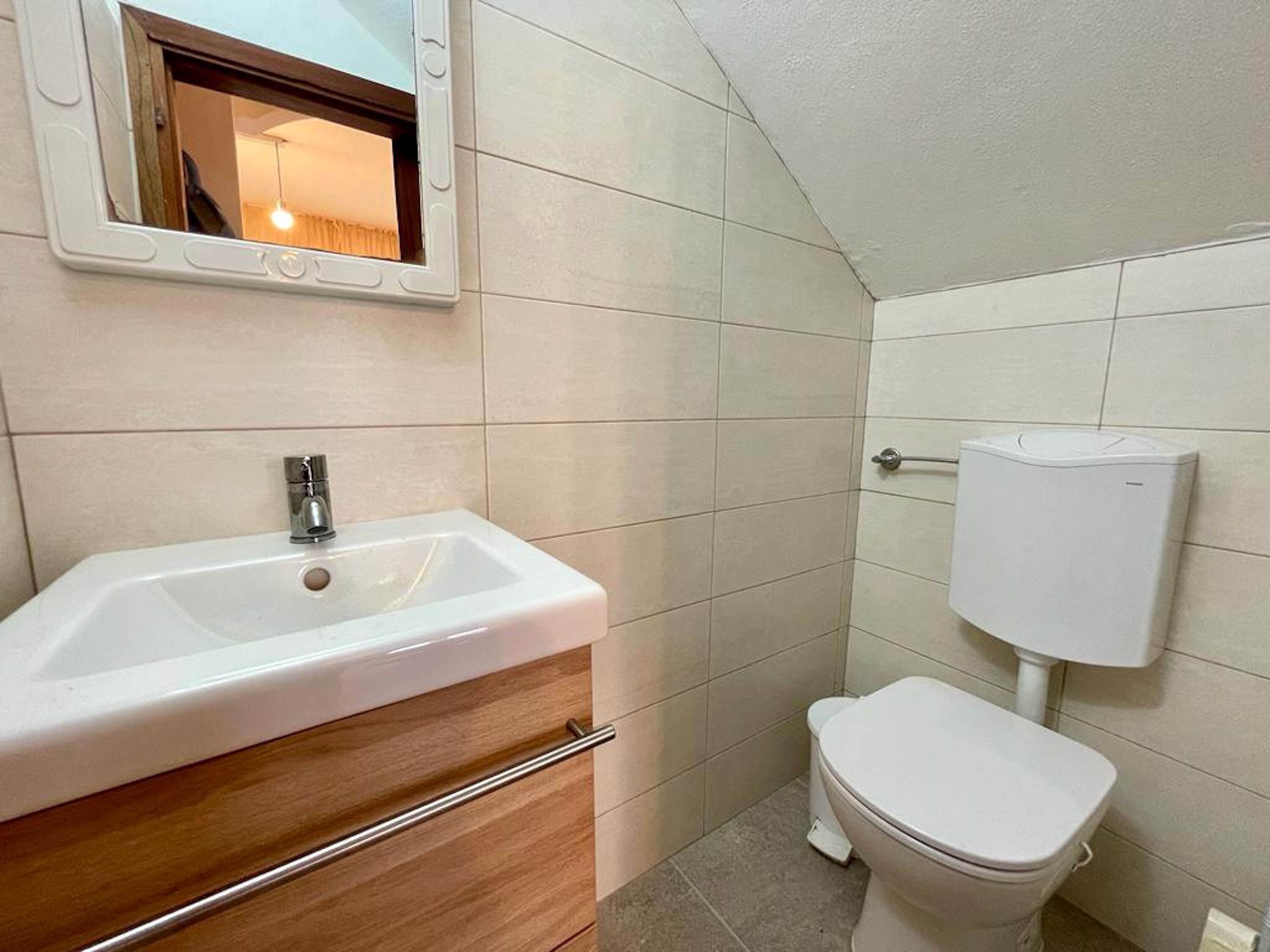 Ein Badezimmer mit einem weißen Waschbecken, einem Holz-Waschtisch und einer Toilette.