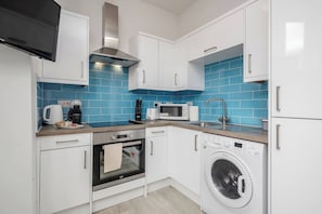 A compact kitchen with white cabinets, a microwave, a toaster, a kettle, and a washing machine. - 1 Bedroom Apartment With Wifi and Parking (Bedford)
