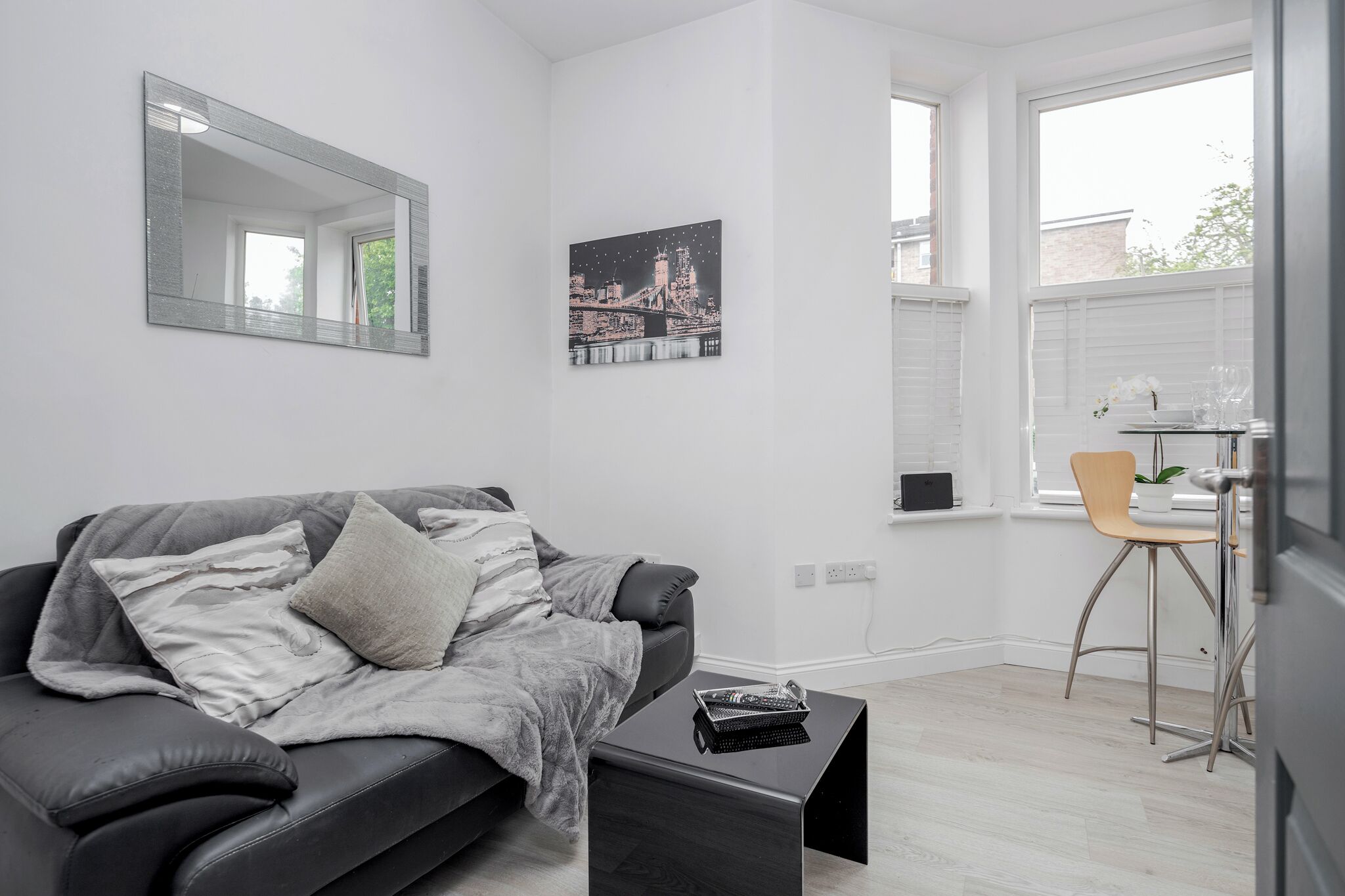 Ein modernes Wohnzimmer mit einem grauen Sofa, einem schwarzen Couchtisch, einem Stadtbild im Bilderrahmen und einem Fenster mit Blick.