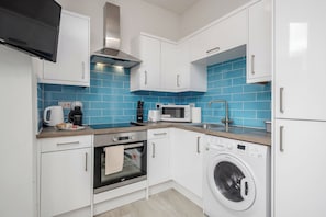 A compact kitchen with white cabinets, a microwave, a toaster, a coffee maker, an oven, and a washing machine.