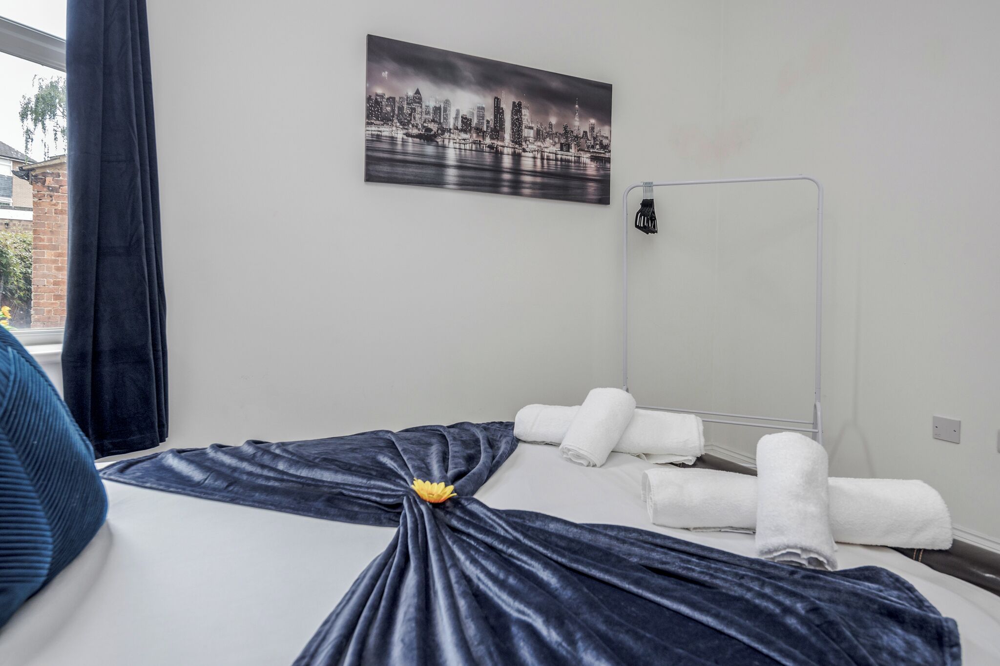 Hotellihuone, jossa on sänky, kaupunkimaisemaa esittävä taulu, peili ja ikkuna, jossa on verhot.