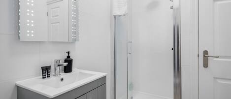 A bathroom with a white sink, a mirror with lights, a shower with a glass door, and a white door.