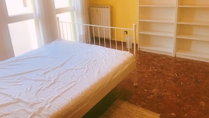 A room with a bed, a radiator, and a white shelving unit.