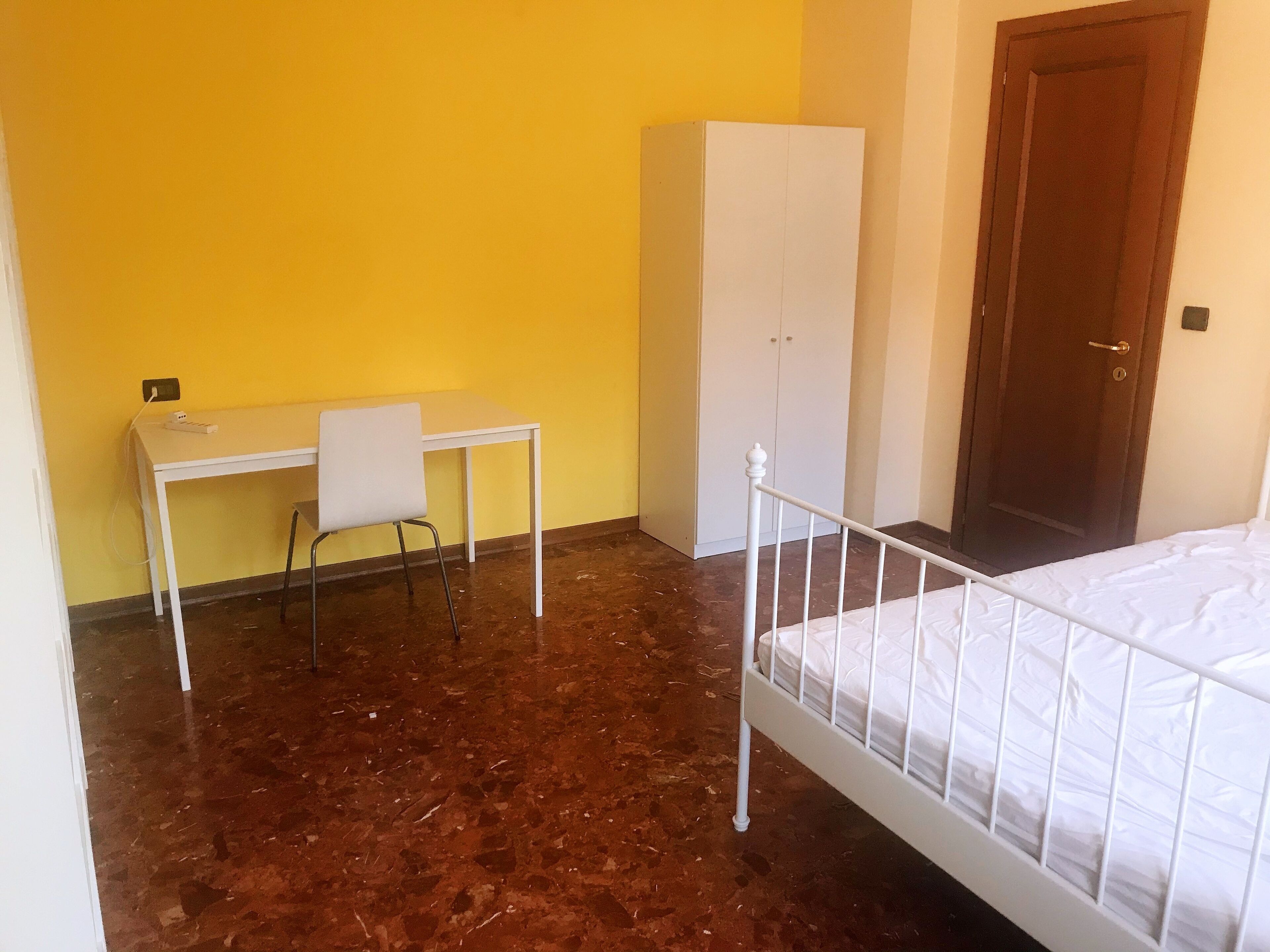 A room with a bed, a desk with a chair, a wardrobe, and a door.