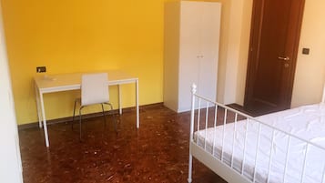 A room with a bed, a desk with a chair, a wardrobe, and a door.