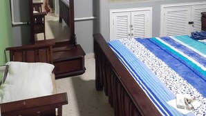 Une chambre à coucher comprenant un lit, une commode, un miroir, une fenêtre avec des rideaux et un radiateur.