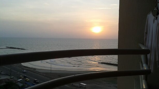 Une vue sur l’océan au coucher du soleil, prise depuis un balcon doté d’une balustrade.
