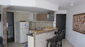 Une cuisine compacte équipée d’un réfrigérateur, d’un four à micro-ondes et d’un évier. On y trouve un petit îlot avec un plan de travail et une chaise. La cuisine est dotée de meubles en bois et d’un pare-feu en carrelage.