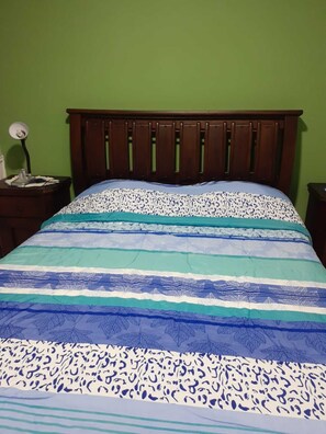 Una cama con una colcha estampada, un cabecero de madera y una mesita de noche con una lámpara.