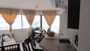 Une chambre d’hôtel compacte dotée d’une kitchenette, d’un coin repas avec une table et des chaises, et de grandes fenêtres avec des rideaux.
