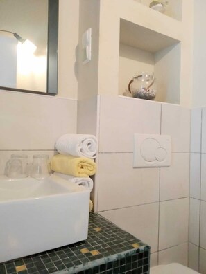 Un baño con lavamanos blanco, un espejo y un perchero con toallas dobladas.