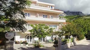 Hotel de dois andares com varanda, área de estar externa e montanhas ao fundo.