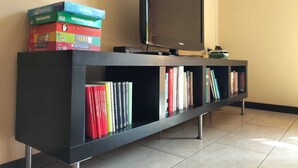 Un meuble noir pour équipements de divertissement, avec un téléviseur à écran plat et une pile de livres aux couleurs vives.