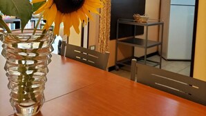 Un coin repas avec une table en bois, un vase en verre contenant un tournesol, et une cuisine en arrière-plan.