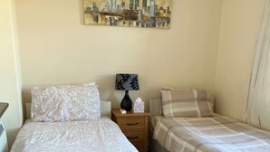 Een hotelkamer met twee bedden, een nachtkastje met een lamp en zakdoekjes, en een stadsgezicht schilderij aan de muur.