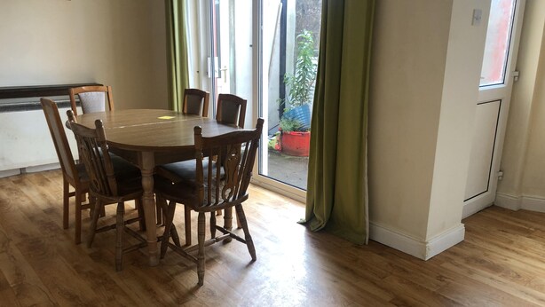 Een eetruimte met een houten tafel en stoelen, een raam met gordijnen en uitzicht op buiten.