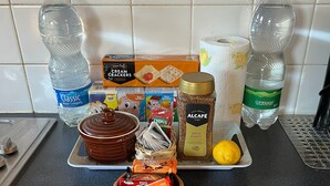 Een aanrecht met verschillende etenswaren en keukengerei, waaronder twee waterflessen, een pot goudgebraad, een kommetje pindakaas en een citroen.