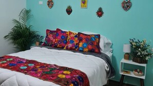 A bedroom with a teal wall, a bed with a colorful quilt, and various wall decorations including star-shaped and heart-shaped items. - El Mezquite Hotel Mexicano Hab 1 la Catrina (Valle de Guadalupe)
