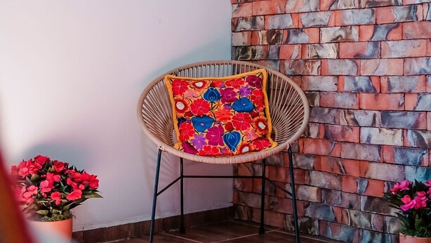 A room with a brick wall, a wicker chair with a colorful cushion, and two potted plants. - El Mezquite Hotel Mexicano Hab 1 la Catrina (Valle de Guadalupe)