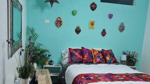 A bedroom with a teal wall, a bed with colorful pillows, a star decoration, and a small table with a bottle and water. - El Mezquite Hotel Mexicano Hab 1 la Catrina (Valle de Guadalupe)