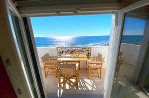A balcony with a table and chairs, overlooking a beach.