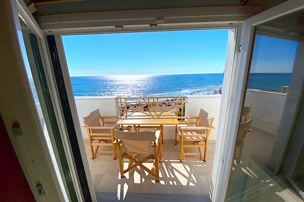 A balcony with a table and chairs, overlooking a beach. - Beachfront Loft Apartment - Agios Gordios Corfu (Corfu)