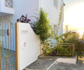 A white building with a sign reading 'NTERIDES,' a metal gate, and a staircase leading to a balcony overlooking the sea.