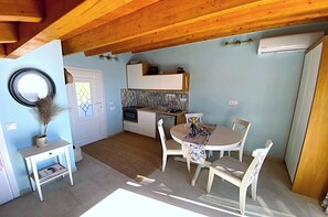 Cocina compacta con comedor, una pequeña mesa y sillas, pared blanca y techo de madera.