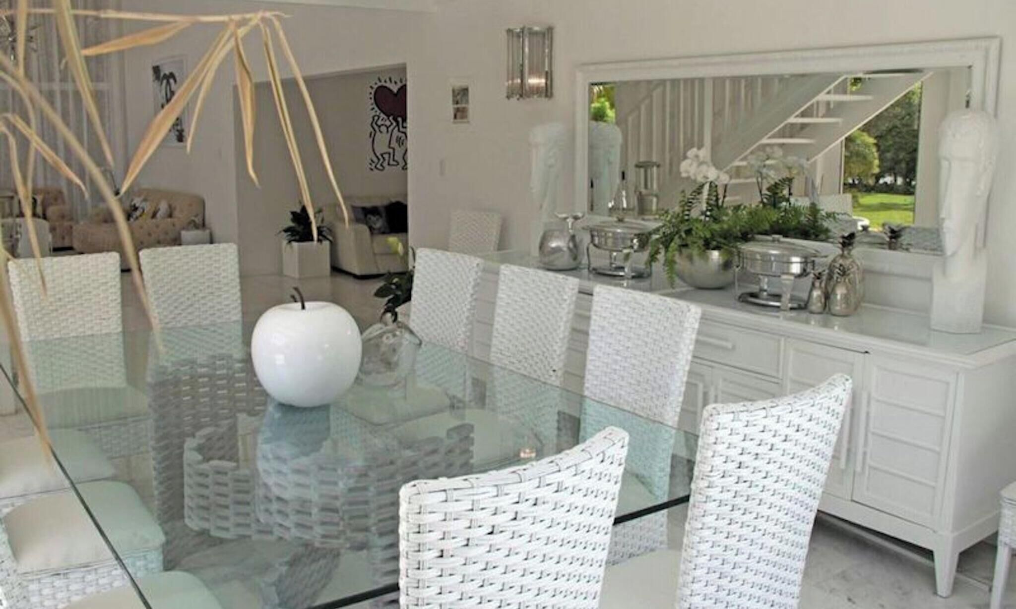 A modern dining area with a glass table, white wicker chairs, and a white cabinet with kitchenware.