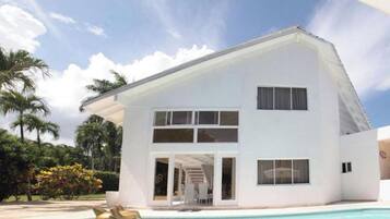 A modern two-story house with a swimming pool, surrounded by tropical vegetation.