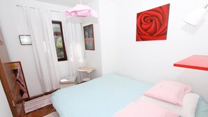 A bedroom with a bed, pillows, a small table, a chair, a window with curtains, and a wall with a painting. - Apollonio Comfort Two-bedroom Apartment (Rovinj)