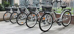 Une rangée de vélos blancs, équipés de paniers noirs, est garée sur une surface pavée.