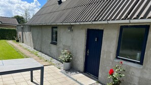 A building with a dark blue door, a window, and a potted plant with red flowers. - A Cozy House to Stay in Vandel (Vandel)