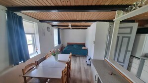 A room with a wooden ceiling, a bed with a green blanket, a dining table with chairs, and a small kitchen area. - A Cozy House to Stay in Vandel (Vandel)