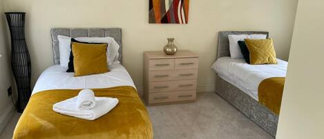 A hotel room with two beds, a bedside table, a lamp, and a painting on the wall.