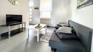 A modern living room with a flat-screen TV, a white coffee table, a grey sofa, and a patterned rug.