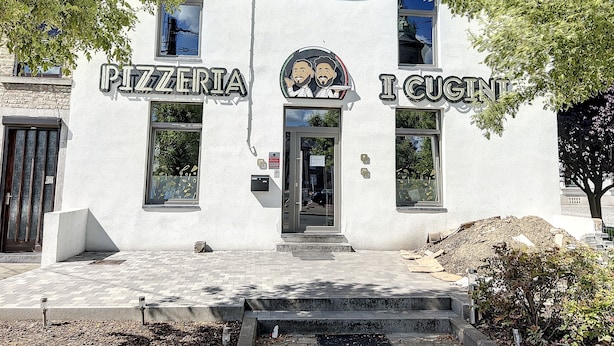 A building with 'PIZZERIA' and 'I CUGNIT' signs, a door, windows, and a paved entrance.