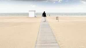 A wooden boardwalk leading to a beach with a small white structure and a lifeguard stand.