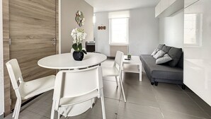 A modern living room with a white sofa, a dining table with chairs, and a large wooden door.