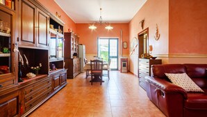A spacious living room with a red leather sofa, a dining table with chairs, and a kitchen area with wooden cabinets and a built-in oven. - Relax in Style in Porto Cesareo's Hidden Gem (Porto Cesareo)