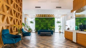 A modern reception area with a wooden wall, a green wall with plants, and a herringbone-patterned floor. - Apartamento S1404 - Downtown Santo Domingo (Santo Domingo)