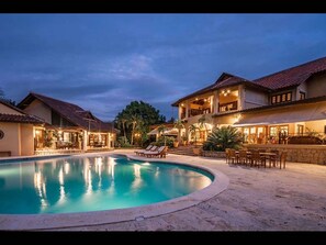 A resort with a swimming pool, outdoor seating, and a well-lit building at dusk.