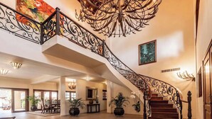 Una gran escalera con barandales negros ornamentales, un candelabro y un cuadro en la pared.