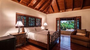 Un dormitorio con techo de madera, una cama con cabecera, dos mesitas de noche con lámparas, un aparador de madera y una ventana con vistas a zonas verdes.