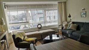 Un soggiorno moderno con un divano, un tavolo da pranzo e vista sulla città attraverso ampie finestre.